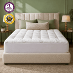 A tufted mattress on a matching upholstered bed frame in a styled bedroom. The mattress is white with a subtle light green botanical pattern, surrounded by green and beige pillows.
